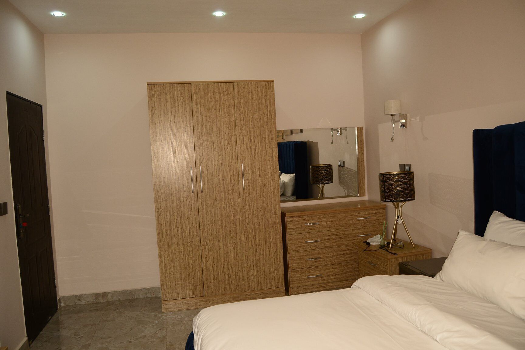 Une chambre à coucher comprenant un lit, une armoire, une commode, un miroir et une table de chevet avec une lampe.