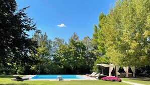 A swimming pool surrounded by lush greenery and a gazebo with seating.