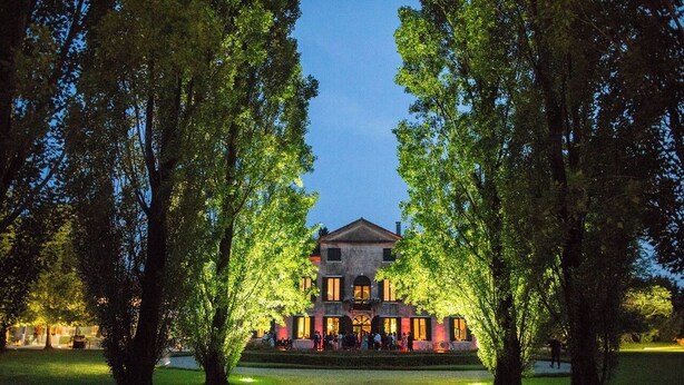A large, historic building with a symmetrical facade, surrounded by a well-maintained lawn and trees, suggesting a formal, possibly heritage-listed venue.