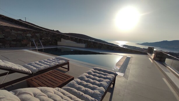 A sunlit outdoor pool area with lounge chairs and a stone wall. - Prime Views A - Peacefull Villa with Private Pool, premium Sea view and Sunsets. (Poseidonia)