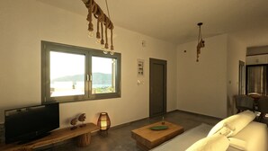 A modern living room with a large window, a television, a sofa, a coffee table, and a hanging light fixture. - Prime Views A - Peacefull Villa with Private Pool, premium Sea view and Sunsets. (Poseidonia)