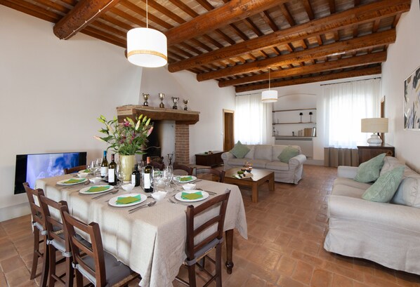 A dining area with a table set for four, a fireplace, and a living room with a sofa and a television.