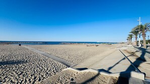 Een breed zandstrand met een betonnen pad en palmbomen.