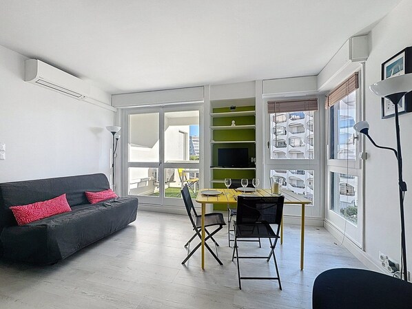 Un salon moderne comprenant un canapé, une table à manger, des chaises et une grande fenêtre donnant sur des immeubles.