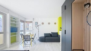Een moderne woonkamer met een grijze bank, een eettafel met stoelen en een boekenkast.