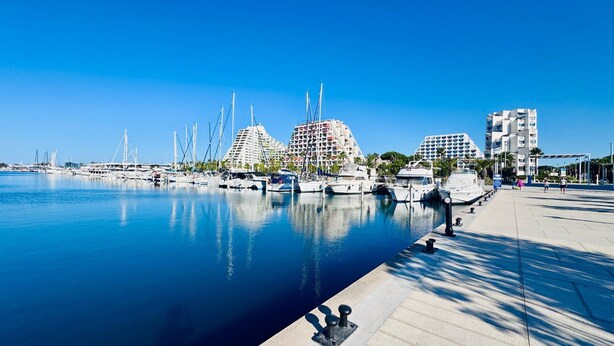 Een jachthaven met aangemeerde jachten, een promenade aan het water en moderne gebouwen met balkons.