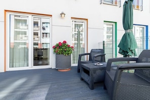 Un balcon agrémenté de meubles en osier, d’une plante en pot et d’un parasol vert.