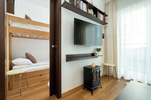 Une chambre avec un lit superposé, un téléviseur fixé au mur, une petite table et un radiateur.