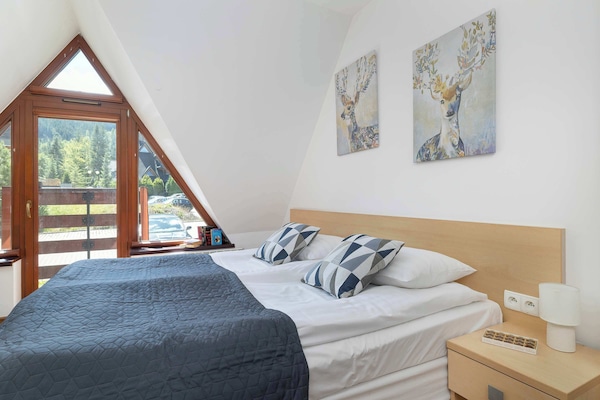 A cozy studio with a large, comfortable bed and a wooden-framed window offering a mountain view.