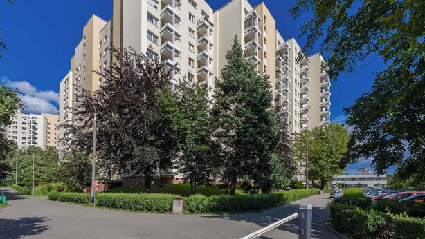 Ein modernes Mehrfamilienhaus mit mehreren Balkonen, umgeben von gepflegter Bepflanzung und einem Parkplatz.
