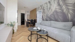 Una sala de estar moderna con un sofá gris, dos mesas redondas, un comedor y un mural grande en la pared.