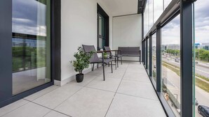 Un balcón con vista a una calle concurrida, una planta en maceta y un área de estar con mesa y sillas.