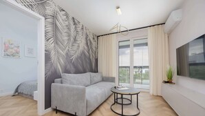 Una sala moderna con un sofá gris, una mesa redonda de centro y un ventanal con cortinas.