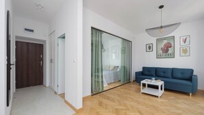 A modern living room with a sofa, a coffee table, and a glass door leading to a bedroom.