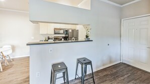 A modern kitchen with a central island, two bar stools, and a dining area with a white table and chairs. - Rocky Mountain Haven w/ king bed, pool & hot tub (Castle Rock)
