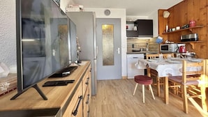 Un espace de vie compact comprenant un téléviseur, des meubles en bois, un coin cuisine et une table à manger.