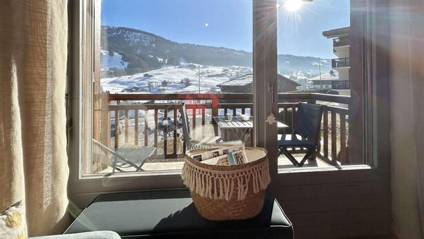 Une pièce avec vue sur un paysage enneigé, visible à travers une grande fenêtre. Dehors, une terrasse en bois est aménagée avec une table et des chaises.