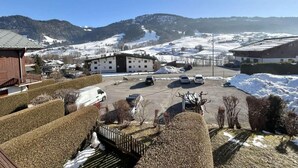 Un parking avec plusieurs voitures, des bâtiments et, au loin, des collines recouvertes de neige.