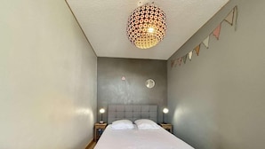 Une chambre à coucher comprenant un lit, deux tables de chevet, un luminaire suspendu et un petit élément décoratif mural.