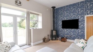 A modern living room with a large sofa, a fireplace, and a television mounted on the wall. - The Gatehouse (Kendal)