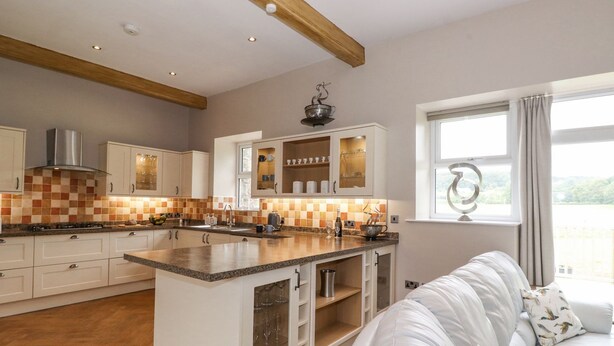 A modern kitchen with a central island, white cabinetry, and a view of a balcony. - The Gatehouse (Kendal)