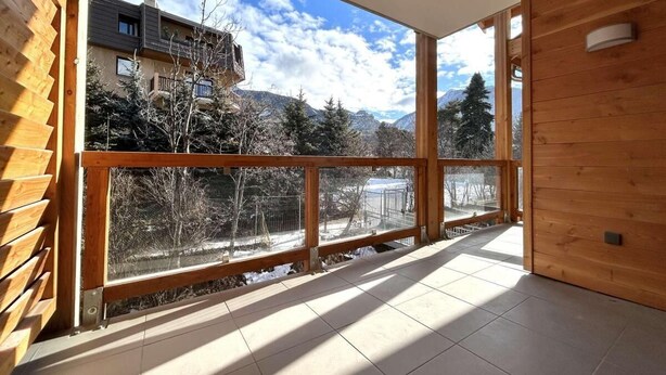 Un balcon spacieux doté de grandes fenêtres offrant une vue sur un paysage montagneux et les bâtiments environnants.