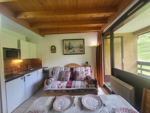 A cozy room with a wooden ceiling, a bed with patterned bedding, a dining table set with plates and glasses, a microwave, and a painting on the wall.