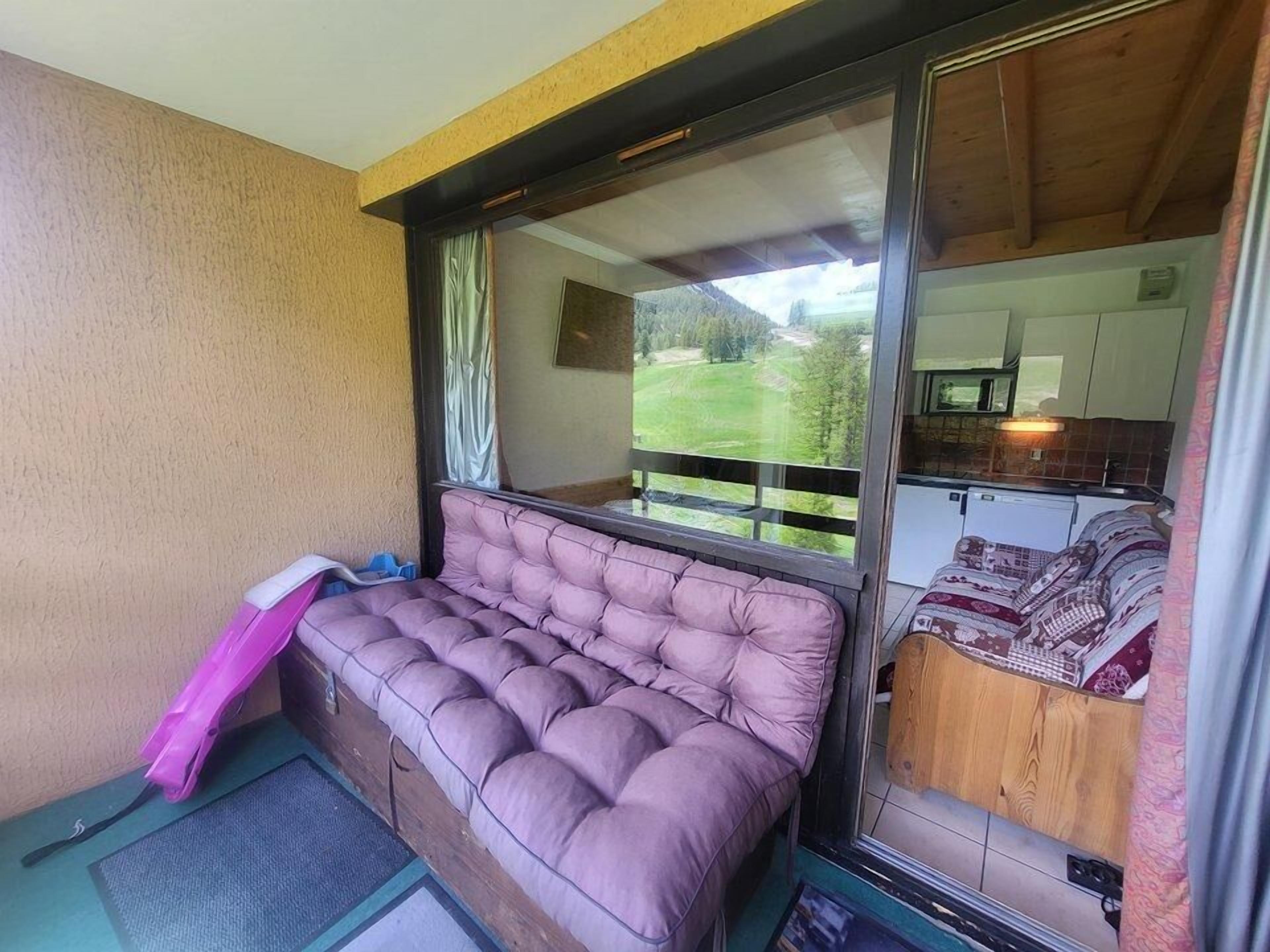 Ein gemütliches Zimmer mit einer gepolsterten Bank, einem kleinen Tisch und Blick auf eine grüne Landschaft durch ein großes Fenster.