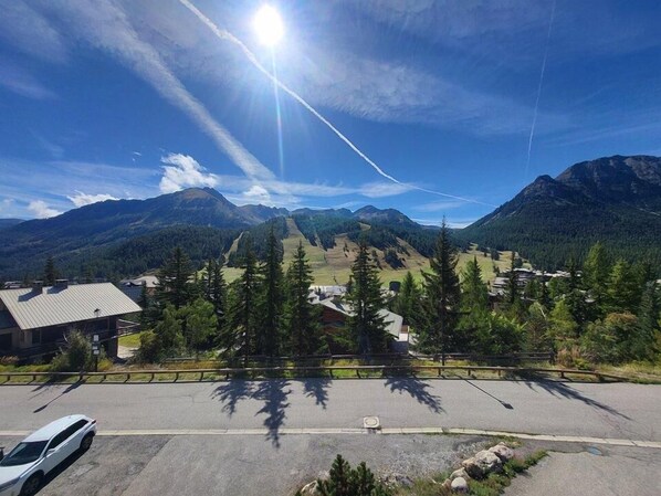 A parking lot with a mountain view, a building with a sloped roof, and a car parked in the foreground.