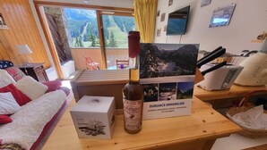 Una mesa de madera con una botella de vino, una caja y un folleto en una habitación con vistas a montañas a través de una ventana.