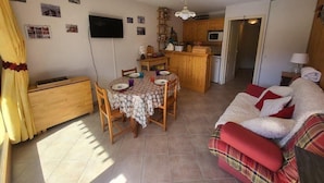 Un espacio habitable compacto con una mesa de comedor, un sofá, una zona de cocina y un televisor montado en la pared.