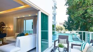 A modern living room with a sofa and chairs, a glass door leading to a balcony with a pool view.
