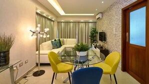 A modern living room with a glass coffee table, yellow and blue chairs, a white sofa, and a brick wall.