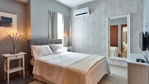 A modern bedroom with a bed, bedside tables, a mirror, and an air conditioning unit.