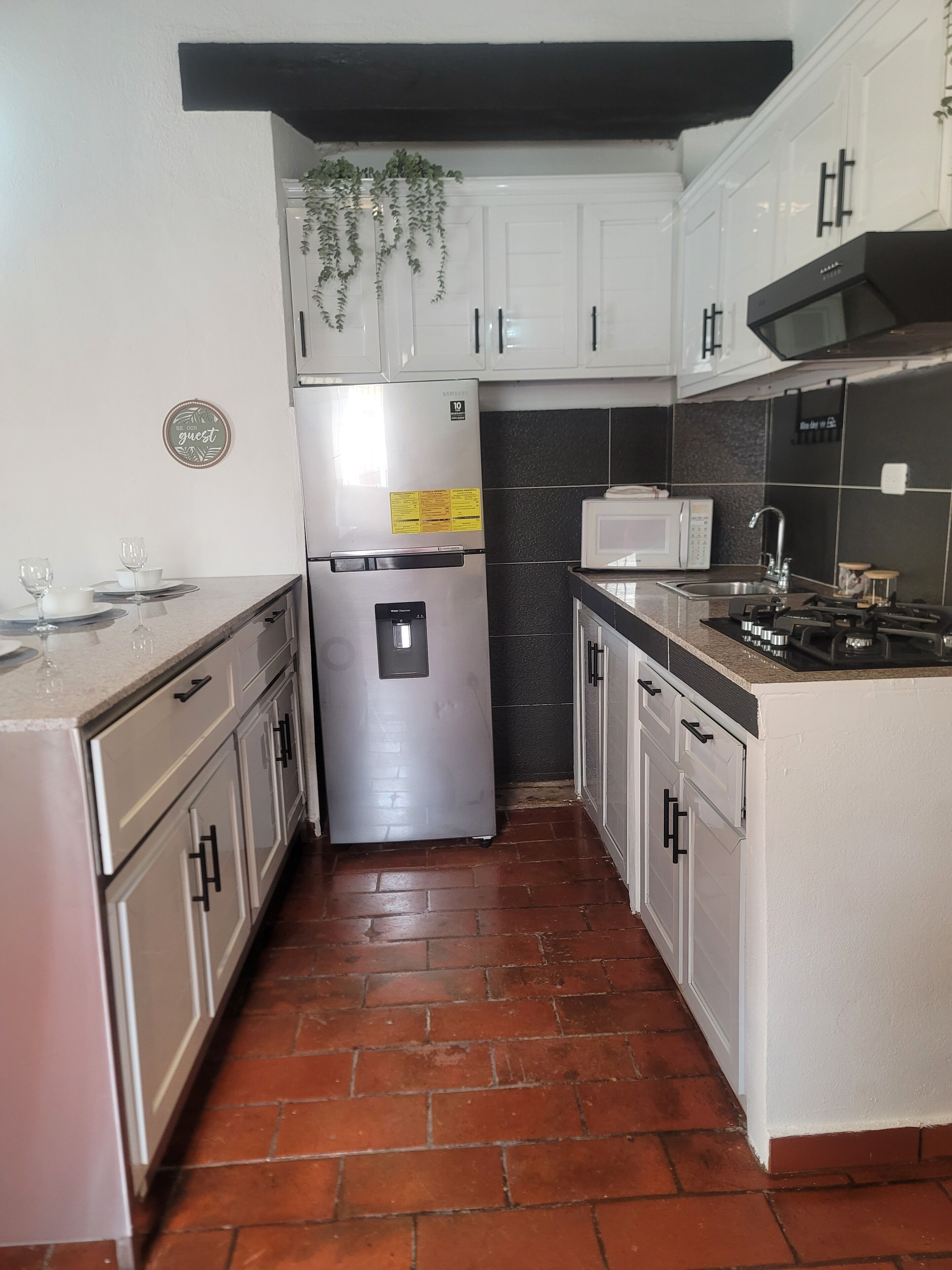 A compact kitchen with white cabinets, a stainless steel refrigerator, a microwave, and a gas stove.