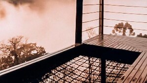 Une terrasse en bois avec une rambarde en métal, donnant sur une étendue d’eau calme et sur des arbres en arrière-plan.
