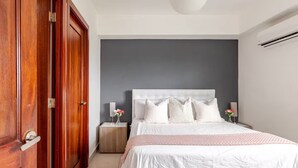 A bedroom with a large bed, wooden wardrobe, bedside tables, and a modern light fixture. - Hermoso apartamento con vista a la ciudad (Santo Domingo)