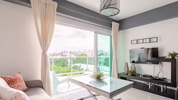 A modern living room with a glass dining table, a sofa, and a TV. - Hermoso apartamento con vista a la ciudad (Santo Domingo)