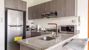 A modern kitchen with a stainless steel refrigerator, a microwave, a coffee maker, and a gas stove. - Hermoso apartamento con vista a la ciudad (Santo Domingo)