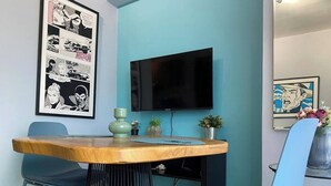 A modern living room with a wooden coffee table, blue chairs, a flat-screen TV, and framed comic book art on the wall. - Atractivo loft (Santo Domingo)