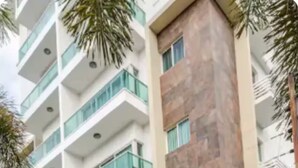 A multi-story building with a modern design, featuring balconies with glass railings, a parking area, and a central column with a stone facade. - Atractivo loft (Santo Domingo)