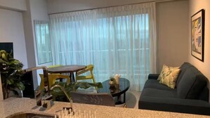 A living room with a dark green sofa, a small round table, and a dining area with yellow chairs. - Atractivo loft (Santo Domingo)