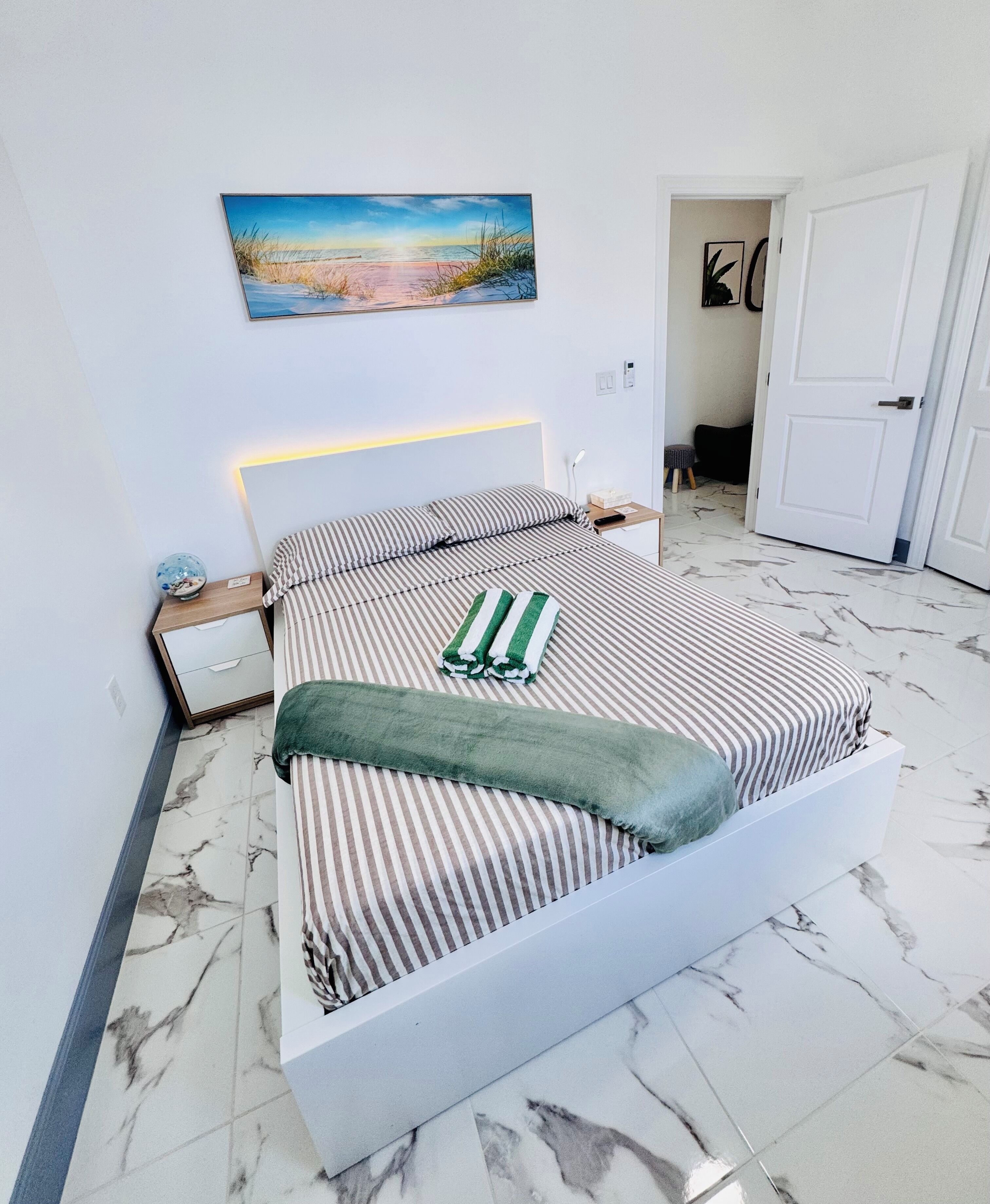 A modern hotel room with a large bed, a nightstand, a wall-mounted painting, and a marble floor.