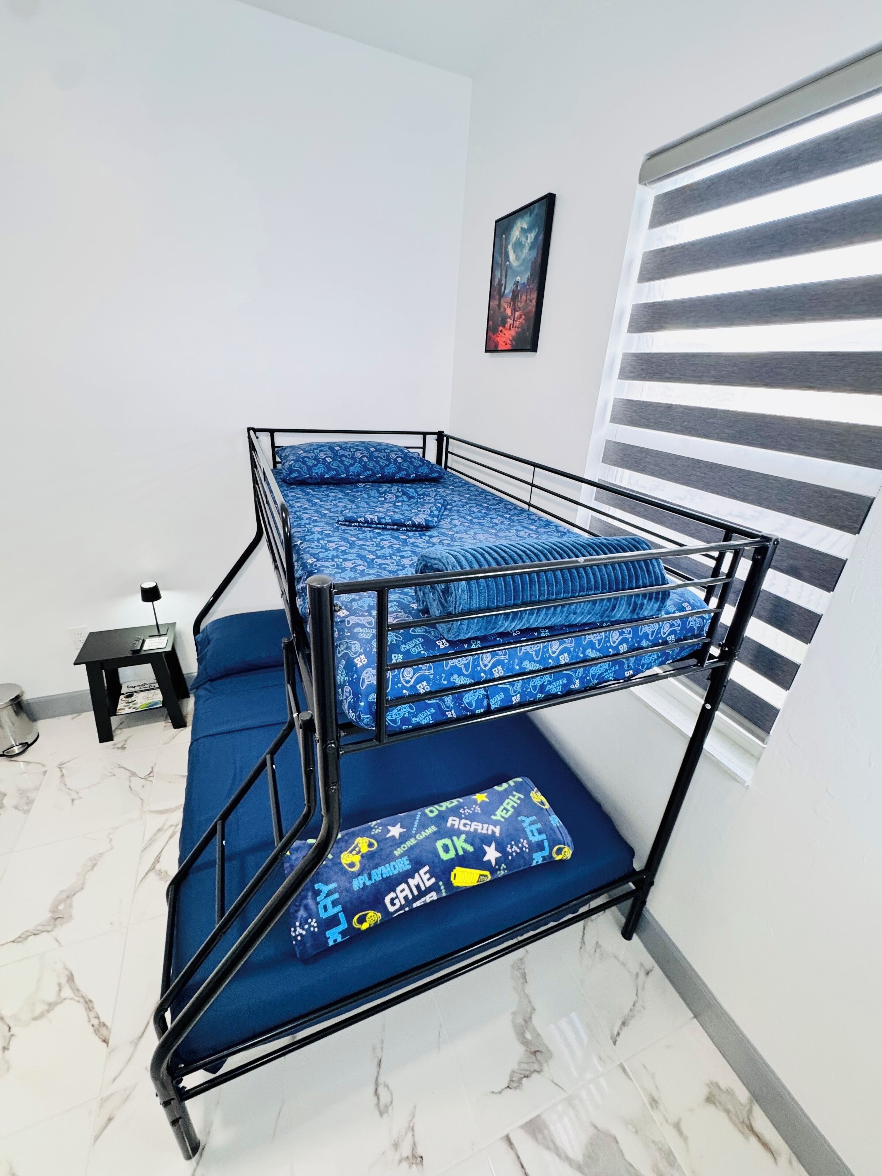 Un lit superposé avec une literie bleue, une petite table avec une lampe et un tableau accroché au mur.
