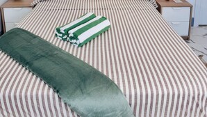 Un letto rifatto con lenzuola a righe, una coperta verde e un quadro raffigurante una spiaggia.