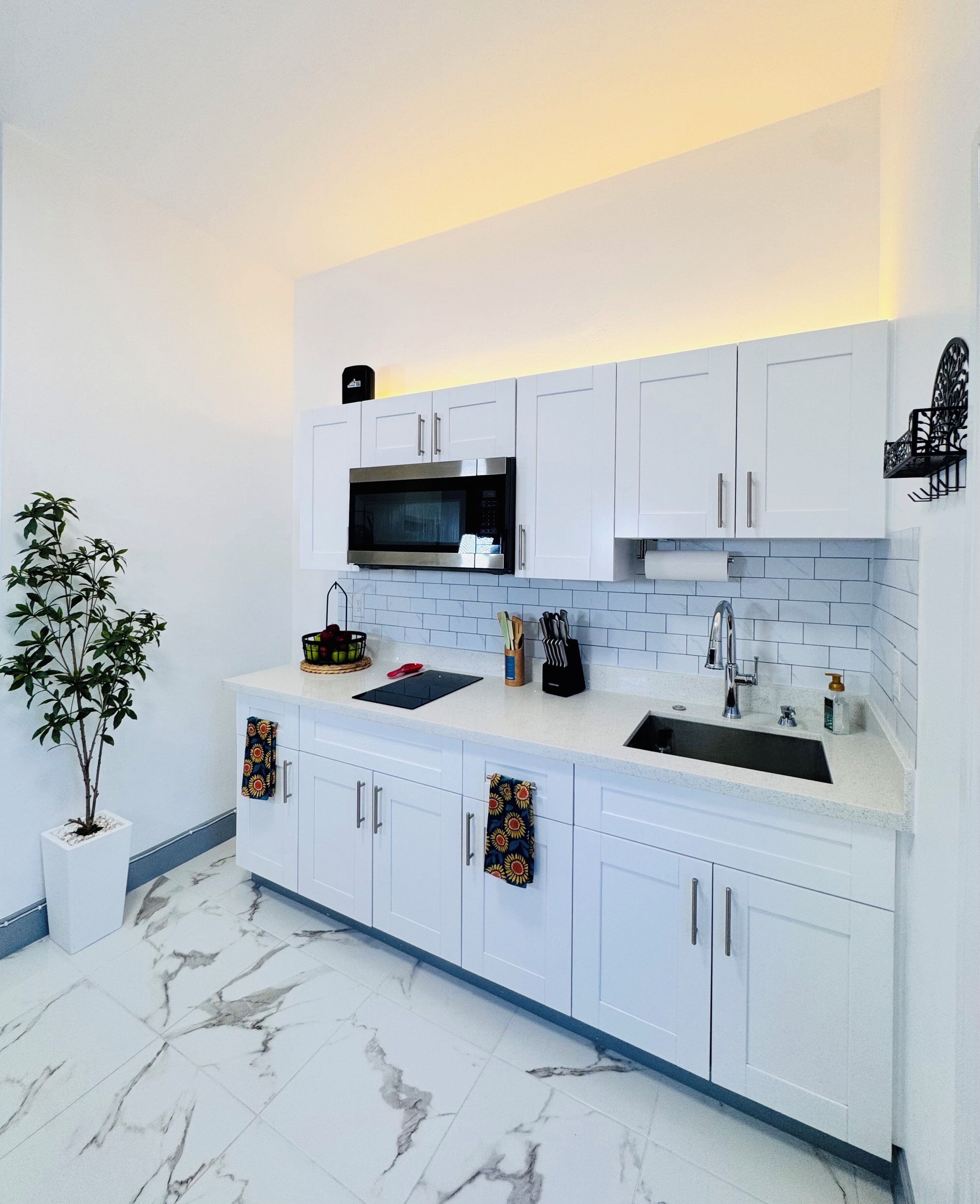 Una cocina moderna con armarios blancos, un microondas negro y un fregadero.