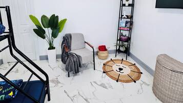 Una habitación con una cama individual, una silla, un tapete redondo, una estantería con libros y una planta en maceta.