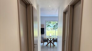 Um corredor com portas de madeira, chão de azulejos e vista para uma sala de jantar com mesa e cadeiras.