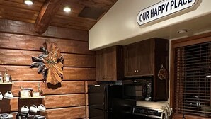A kitchen with wooden cabinets, a large island, coffee machines, and a sign that reads "OUR HAPPY PLACE". - Romantic Winter Escape/Hot tub in Heaven (Pine)
