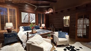 A cozy log cabin bedroom with a large bed, a sitting area with a chair and a small table, a dresser, and a wardrobe with a mirror. - Romantic Winter Escape/Hot tub in Heaven (Pine)